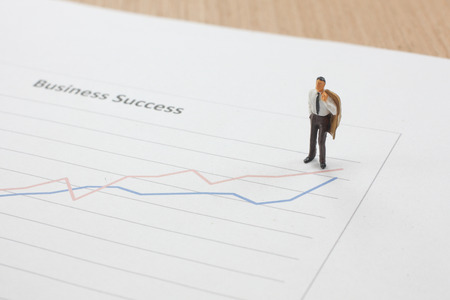 Miniature figure Businessman standing on the report graph  of  business direction strategy and success conceptの写真素材