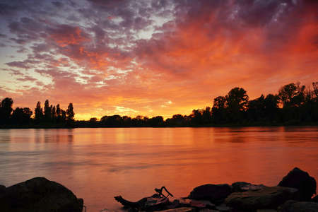 A fantastic sunset at river Rhine. Orange and red clouds reflecting in the water. Long exposure. Germany, Baden-Wurttemberg.の写真素材