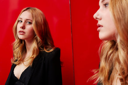 Beautiful woman looking in mirror in red roomの写真素材
