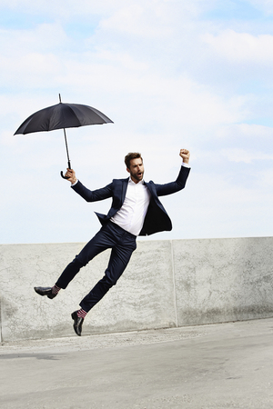 Ecstatic jumping businessman with umbrellaの写真素材