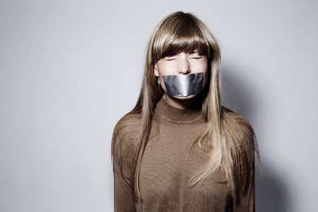 Young blond woman with taped mouth, eyes closedの写真素材