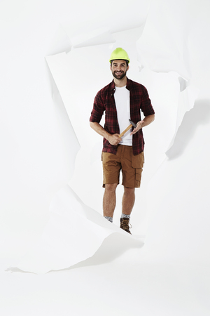 Happy builder with hammer emerging through torn pageの写真素材