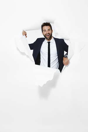 Businessman emerging from paper, portraitの写真素材