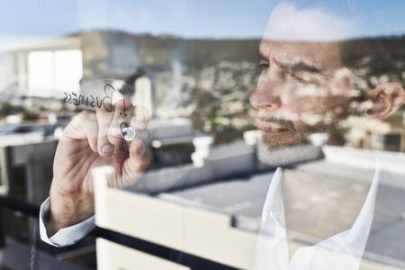 Businessman writing on window, close upの写真素材
