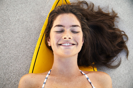 Surfer girl lying on board on beach, smilingの写真素材