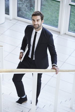 Sharp suited businessman holding laptop on stepsの写真素材