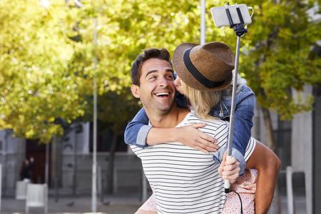 Kissing selfie couple in city, smilingの写真素材