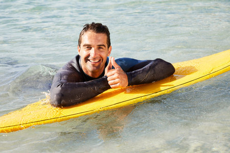Portrait of surfer with thumbs up on surfboard, smilingの写真素材