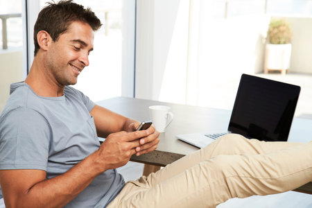 Texting guy relaxing at desk at home, smiling