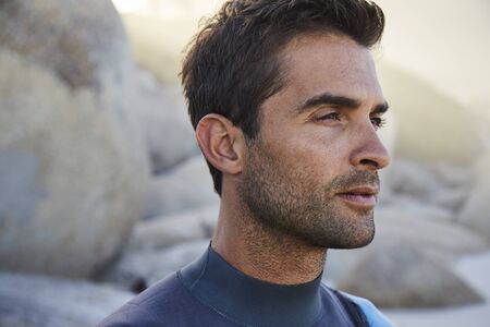 Good looking guy in wetsuit on beach, looking awayの写真素材