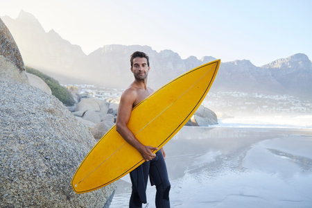 Surfer dude standing on beach, looking at camera