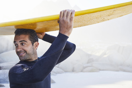 Surfer dude in wetsuit holding board on head, smilingの写真素材