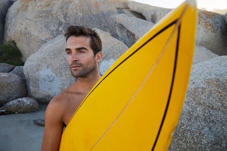 Handsome surfer dude with board on beach, looking away