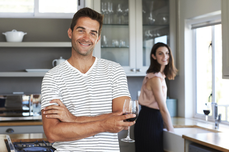 Happy guy in striped t-shirt holding wine in kitchenの写真素材
