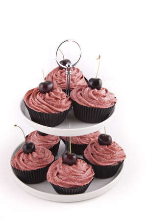 Chocolate flavored cupcakes, with red frosting and a cherry on top, on a cupcake stand on white backgroundの写真素材