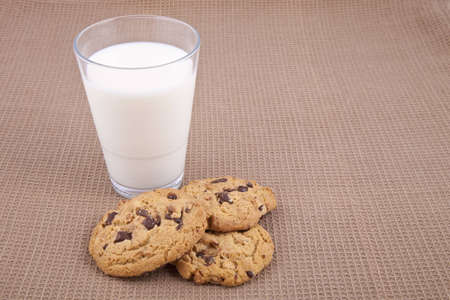 Chocolate chip cookies and a glass of milk, on a brown cotton tableclothの写真素材