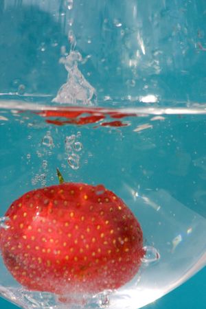 strawberry is fallen down in water glass on blue backgroundの写真素材