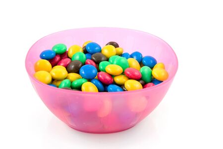 pink plastic bowl with colorful chocolate candy isolated on white backgroundの写真素材