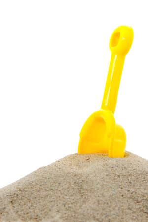 Sand pile with yellow toy shovel over white backgroundの写真素材