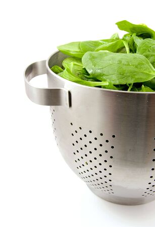 colander filled with fresh spinach over white backgroundの写真素材