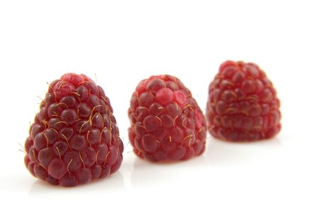 Three fresh raspberries in a row over white backgroundの写真素材