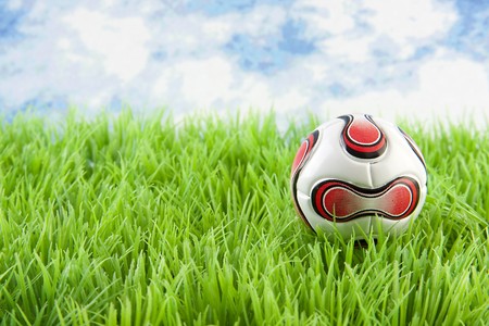 Soccer ball on grass against blue cloudy skyの写真素材