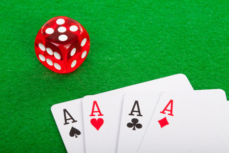 winning poker hand of four aces playing cards and red dice on green background
