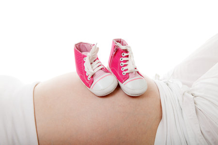 Pregnant belly with little pink shoes over white background