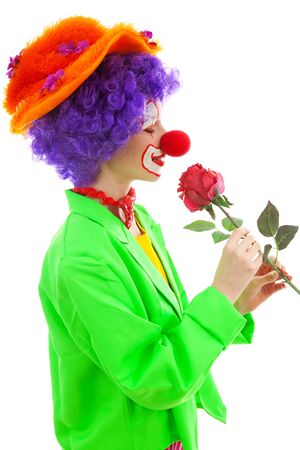 portrait of child dressed as colorful funny clown smelling red rose over white backgroundの写真素材