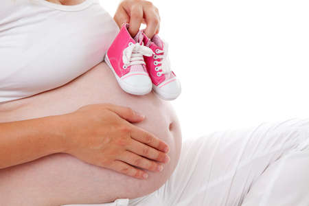 Woman is holding little pink shoes over pregnant belly on white backgroundの写真素材