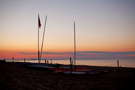 Silhouettes of boats and people on the beach by sunsetの写真素材