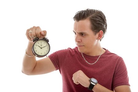 Young man is angry at alarm clock over white backgroundの写真素材
