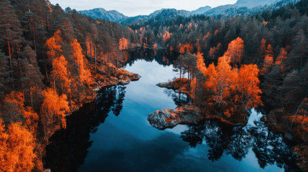 A breathtaking autumn scene featuring vibrant orange trees along a peaceful body of water, reflecting the stunning landscape and majestic mountains.の素材