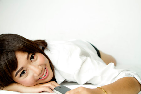 Sexy asian girl with white dress using mobile phone in the bed.の写真素材