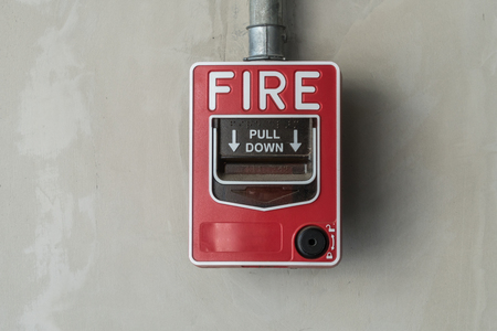 Red fire switch on gray concrete wallの写真素材