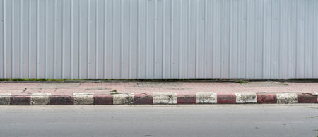 Gray metal sheet fence with concrete sidewalk and asphalt road