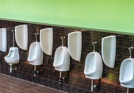 White ceramic urinals on brown tiles wall in men's toiletの写真素材