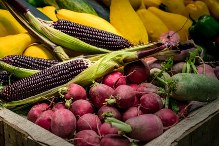 Purple corn on pile of vegetables and fruit in wood tray