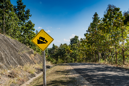 Yellow Steep hill traffic sign with green trees and blue skyの写真素材