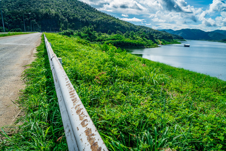 Asphalt country road with metal hedge on green mountain and blue sky backgroundの写真素材