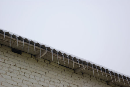 Icicles hanging dangerously down from eaves of the roof of an old house