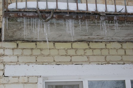 Icicles hanging dangerously down from eaves of the roof of an old houseの写真素材