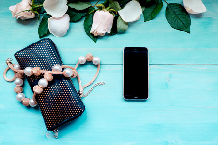 Spring background layout on a blue wooden background with flowers and rose petals phone purse and beads accessories on a wooden backgroundの写真素材