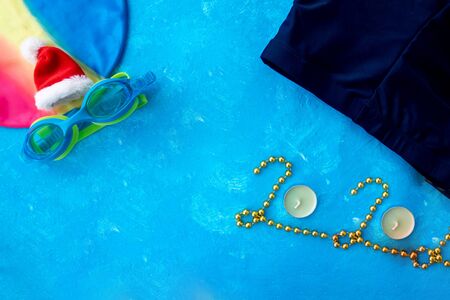 Happy New Year 2020 written by gold stones on floor tile background with mustache and santa hat close up on blue swimming pool background with space for your textの写真素材
