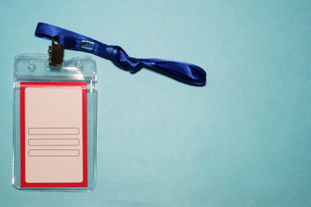 close-up plastic case of neck label hanging isolated on blue background, blank name-tag label and...