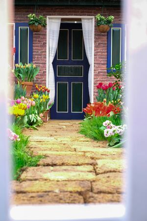 the path from the fence to the house is dotted with flowers tulips on the right and left. small white wooden fence near a country house. concept of a country house, fence, beautiful fence.の写真素材