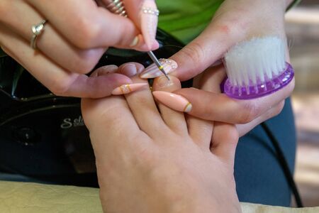 Step-by-step pedicure at home. Removal of rough skin and cuticles by the device during a pedicure at home. Concept of toenail careの写真素材