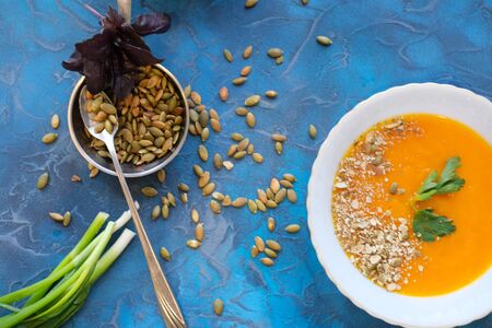 pumpkin soup with green parsley and young green onion feathers with pumpkin and corn in the background, with toasted pumpkin seeds decorated with purple Basil on a rich blue backgroundの写真素材