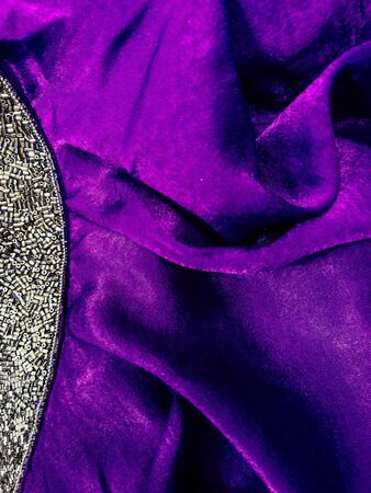 The texture of a lilac folded fabric with a shiny border of beads with rhinestones. Background texture, pattern. lilac fabric with metallic sequins.の写真素材