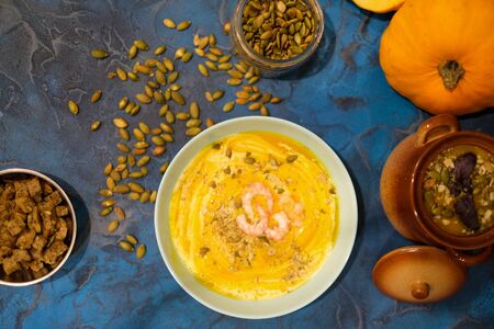 Autumn food - pumpkin soup with cream, shrimps and seeds in bowls on table. pumpkin soup decorated with pumpkin seeds and toasted crackers on a dark blue background. Served for dinner View from aboveの写真素材
